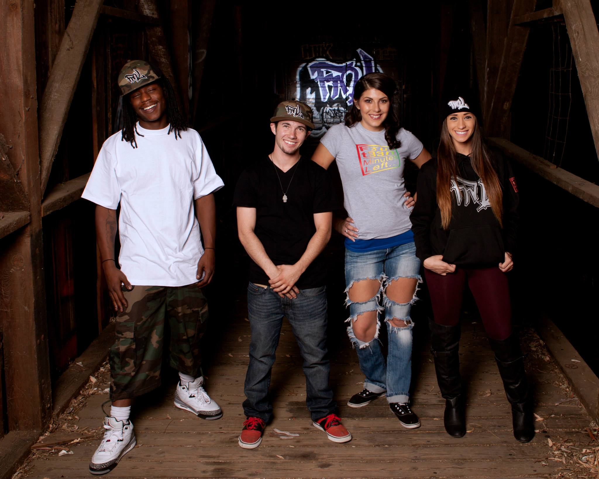Four people posing in Fourt33n Minutes Left... gear together in a rustic wooden setting with a logo in the background.